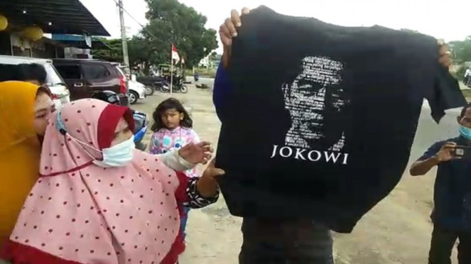 Warga menunjukkan souvenir kaos bergambar Jokowi yang dilempar Presiden