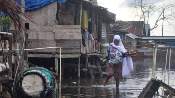 Seorang wanita paruh baya berjalan melintasi genangan air banjir akibat rob yang sering melanda dua desa Di Kecamatan Sirenja, Kabupaten Donggala, Sulawesi Tengah.