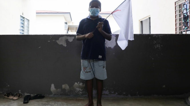 Seorang anak laki-laki memegang bendera putih yang digantungkan keluarganya untuk meminta bantuan selama lockdownÂ Malaysia. (Reuters:Â Lim Huey Teng)