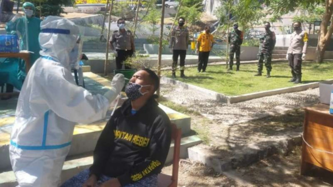 Aparat Polisi dan TNI, Kamis, 22 Juli 2021, mengawasi pelaksanaan tes secara cepat antigen kepada seorang pria yang sempat mengambil paksa jenazah pasien COVID-19 di Kupang, Nusa Tenggara Timur.