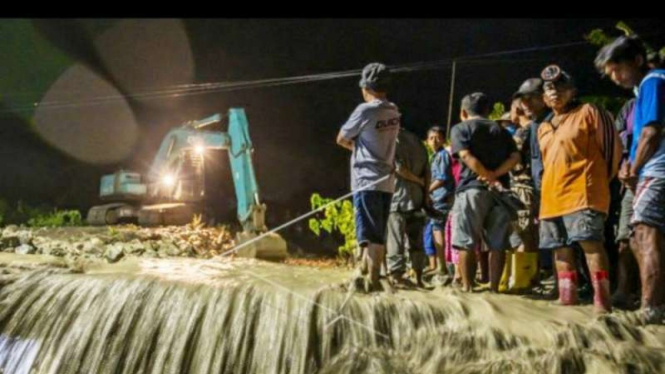 Sejumlah warga menyaksikan alat berat membersihkan material lumpur yang memenuhi aliran sungai dan jalan di Desa Beka, Sigi, Sulawesi Tengah, Jumat malam, 3 September 2021.