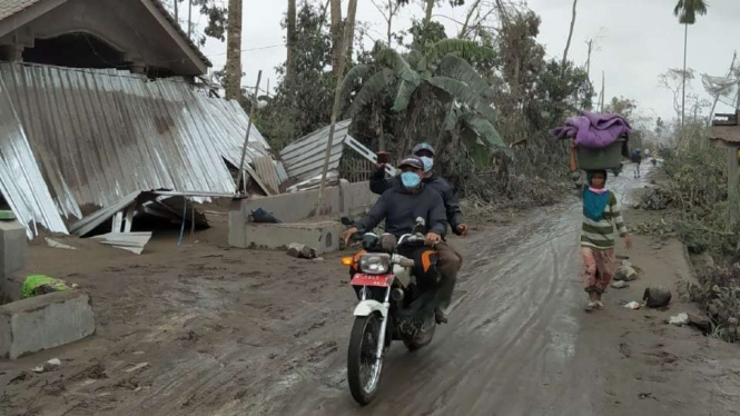 Dua orang petugas bersepeda motor berpatroli melintasi jalan desa di Lumajang, Jawa Timur, Senin, 6 Desember 2021, menyusul erupsi Gunung Semeru pada Sabtu pekan lalu.