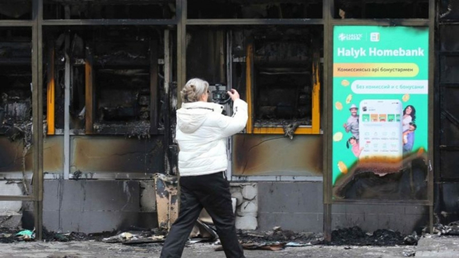 Seorang perempuan merekam sebuah bangunan, yang terbakar di Almaty, Kazakhstan.