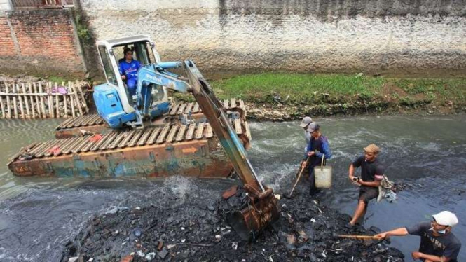 Petugas menggunakan alat berat saat mengeruk tanah dan lumpur di Kali Mampang.