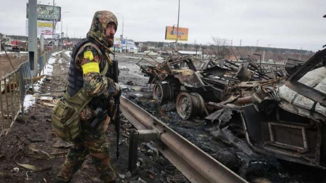 Pria dengan senjata dan kendaraan perang Rusia yang hancur di Bucha, Ukraina