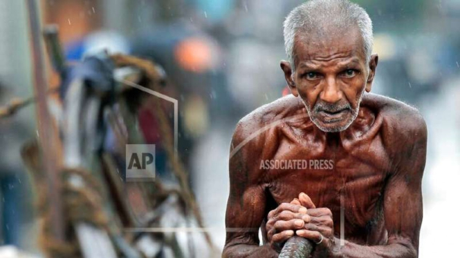 Pekerja kasar berusia tua di Sri Lanka mendorong pedati saat hujan tahun 2012