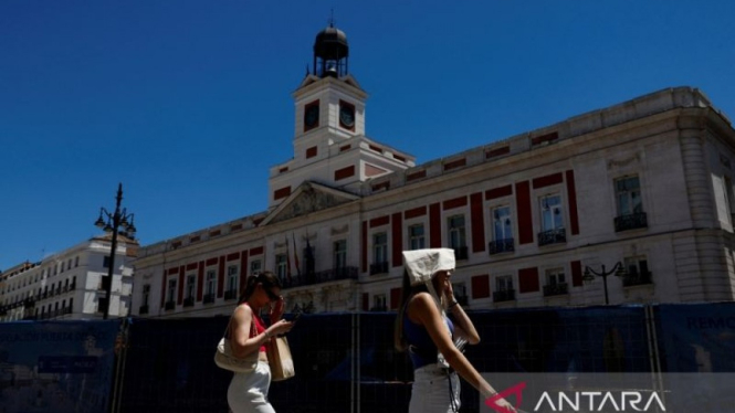 seorang wanita menutupi kepalanya dengan tas saat berjalan di Alun-Alun Puerta del Sol pada hari yang panas saat Spanyol bersiap menghadapi gelombang panas di Madrid, Spanyol.