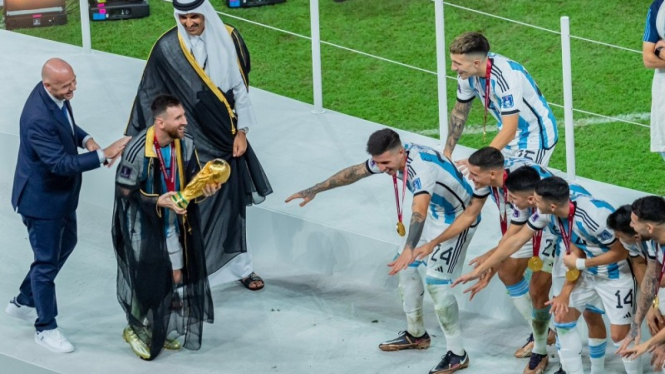 Lionel Messi mengenakan jubah dan memegang trofi Piala Dunia