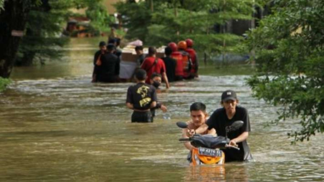 Warga menuntun sepeda motornya melewati banjir di Perumnas Antang, Makassar, Sulawesi Selatan, Senin, 26 Desember 2022.
