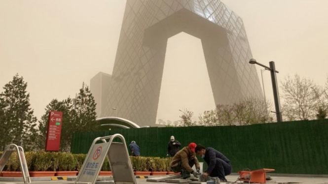 Pekerja konstruksi terlihat di depan kantor pusat CCTV terselubung debu saat kota terkena badai pasir di Beijing, China.