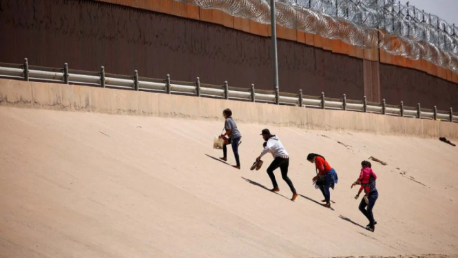 Imigran pencari suaka berjalan dekat dinding perbatasan setelah menyeberangi Sungai Rio Bravo, di El Paso, Texas, Amerika Serikat.