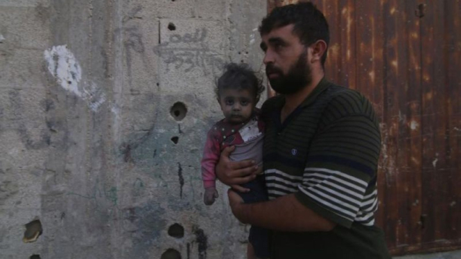 Seorang warga menggendong anaknya usai serangan Israel di Kota Rafah, Jalur Gaza