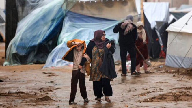 Warga Palestina berjalan di tengah hujan di kamp pengungsian di Rafah, Gaza.