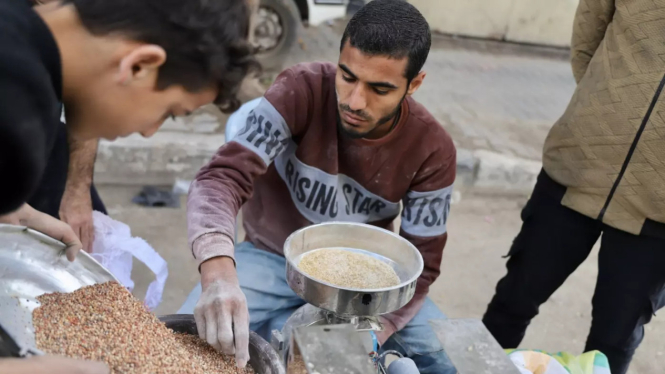 Seorang pria Palestina menyaring biji-bijian di Gaza di tengah kekurangan pangan