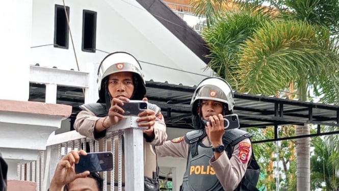 Dua aparat kepolisian terlihat merekam momen mahasiswa ricuh saat demo di Kantor DPRD NTB, Rabu, 16 Oktober 2024 (Satria)