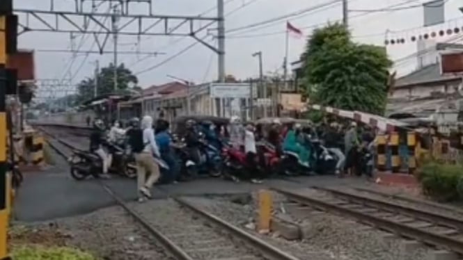 Pengendara sepeda motor menerobos jalur perlintasan kereta saat palang tertutup.