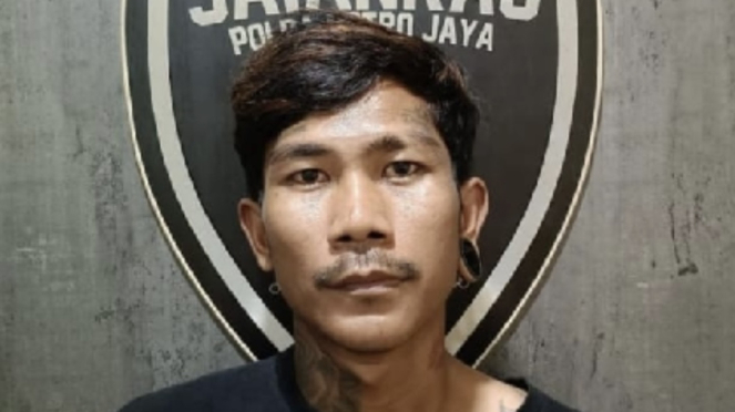 Pelaku, RS terlihat mengenakan kaus hitam dengan rambut pendek yang dicat cokelat. Tato terlihat di leher kanannya, sementara telinga kirinya ada tindikan.