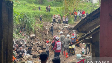 Petugas membersihkan material tembok penahan tanah yang menimpa rumah warga